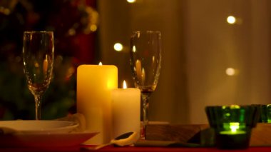 Yeni yılı ya da Noel 'i kutlamak için dekore edilmiş rahat bir oda. Mumlar festival masasında yanıyor, tabaklar ve bardaklar yerleştirildi. Az ışık. İç detayları kapat. Yavaş çekim.