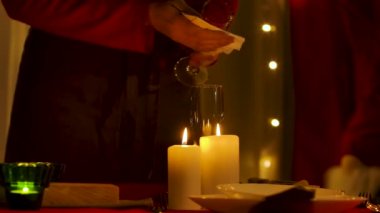 Kadın yeni yıl ya da noel kutlaması için dekore edilmiş odanın arka planında tabak düzenler, şampanya bardaklarını siler. Şenlik masasında mumlar yanıyor. Az ışık. Eller yukarı. Yavaş çekim.