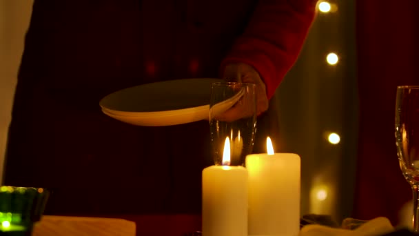 Vrouw veegt witte borden tegen de achtergrond van de kamer versierd voor de viering van nieuwjaar of kerst. Kaarsen branden op feestelijke tafel naast glazen. Weinig licht. Handen dicht. Langzame beweging. — Stockvideo