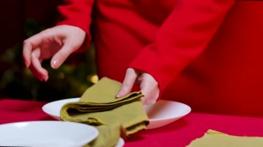 Kırmızı elbiseli kadın, yılbaşını ya da Noel gecesini kutlamak için süslenmiş şenlik masasında yatıyor. Tabakları, çatal bıçakları ve şampanya kadehlerini ayarlar. İç detayları kapat. Yavaş çekim.