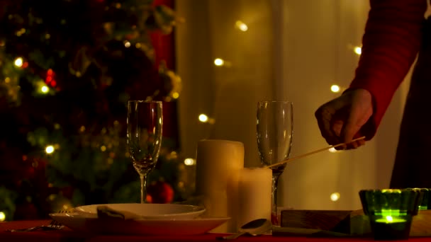 Mujer enciende velas en la mesa festiva con platos arreglados. Casa acogedora habitación, decorada para Año Nuevo o celebraciones de Navidad. Preparándose para la noche festiva. Con poca luz. Las manos cerca. Movimiento lento. — Vídeos de Stock