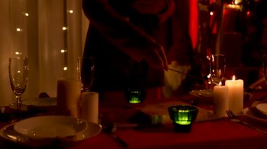 Kadın sofraya mum yakar, bulaşıkları da hazırlar. Yeni yıl ya da Noel kutlamaları için dekore edilmiş rahat bir oda. Şenlik gecesine hazırlanıyorum. Az ışık. Eller yukarı. Yavaş çekim.