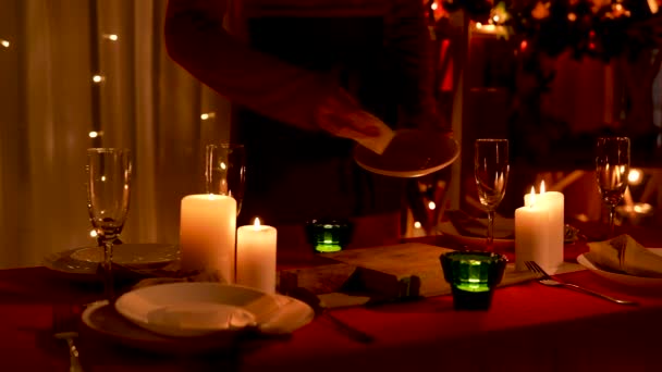 Femme essuie plaques blanches sur fond de pièce décorée pour la célébration du Nouvel An ou de Noël. Les bougies brûlent sur la table de fête à côté des verres. Lumière faible. Les mains en l'air. Mouvement lent. — Video