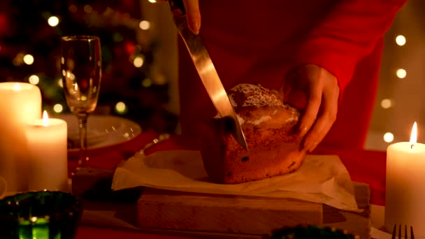 Γυναίκα κόβει παραδοσιακό σπιτικό cupcake σε γιορτινό τραπέζι με πιάτα και ποτήρια σαμπάνιας τοποθετημένα. Home room, διακοσμημένο για τον εορτασμό της Πρωτοχρονιάς ή των Χριστουγέννων. Χαμηλό φως. Κλείσε. Αργή κίνηση. — Αρχείο Βίντεο