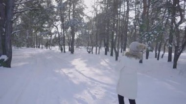 Kışın pardösülü kız, karlı kış ormanlarında yol boyunca yürür. Genç bayan etrafa neşe ve gülümsemeyle bakıyor. Ormanda çok kar var. Karlı kış. Güneşli soğuk bir gün. Yavaş çekim.