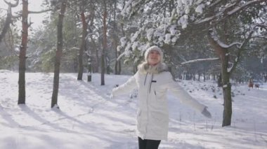 Gülümseyen mutlu kız yağan karda seviniyor. Beyaz kar taneleri güneş ışınlarında parıldıyor. Karla kaplı ağaçlardan düşen kar. Güzel kış doğası. Kış ormanında yürü. Yavaş çekim.