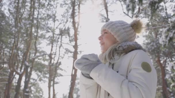 Вид знизу мила заморожена дівчина в зимовому одязі і капелюх зігріває руки в рукавичках. Дівчина насолоджується морозним сонячним днем. Прекрасна зимова природа вкрита снігом. Близько. Повільний рух . — стокове відео
