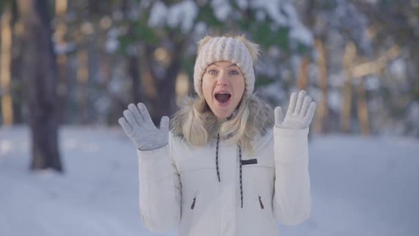 Портрет милой девушки в теплой зимней одежде, смотрящей в камеру с восторгом и удивлением. Молодая женщина позирует на открытом воздухе на размытом фоне снежного леса. Закрывай. Медленное движение. — стоковое видео
