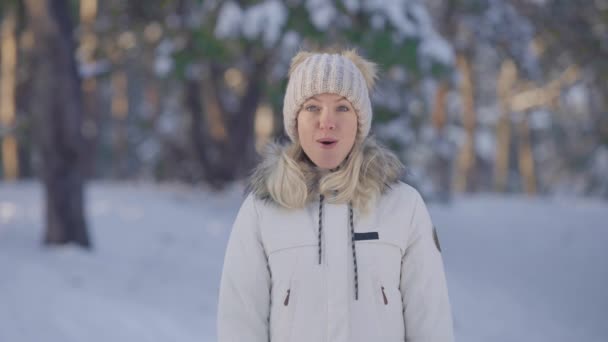 Ritratto di ragazza carina in caldi vestiti invernali guardando la fotocamera con wow delizia e sorpresa. Giovane donna in posa all'aperto su sfondo sfocato di foresta innevata. Chiudete. Rallentatore. — Video Stock