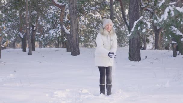 Boldog aranyos lány meleg téli ruhák ugrás, szórakozás és dobott hó. Havas téli szórakozás a friss fagyos levegőn a napsütéses napon. Gyönyörű háttér havas természet fenyves erdőben. Lassú mozgás.. — Stock videók