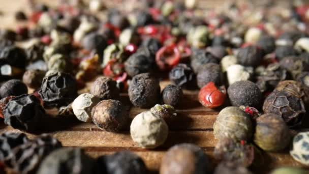 Auf dem hölzernen Küchentisch schwenkt die Kamera über eine bunte Mischung aus scharfen Pfefferkörnern. Großaufnahme von rosa, weißen und schwarzen duftenden Paprika, die auf den Tisch fallen. Fallende Samen von Bittererbsen in Zeitlupe. — Stockvideo