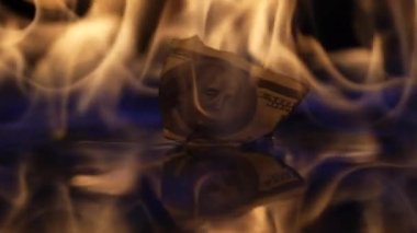 Yangının alevlenmesi ve yanması buruşmuş kağıt dolarları aydınlatıyor. Para siyah bir arkaplanda yanar, paralar alevlerle kaplanır, para birimi ateşe verilir. Yaklaşın, ağır çekim..