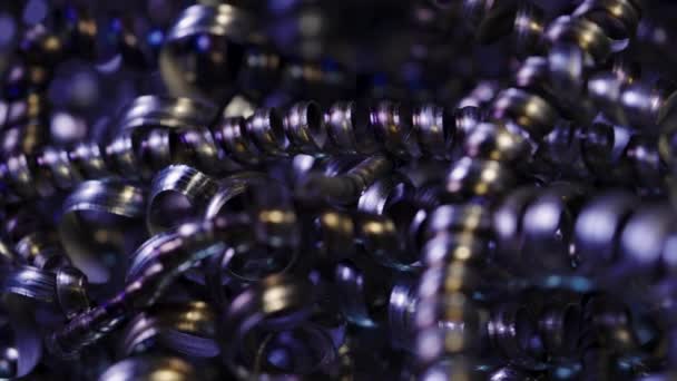 Camera pans along shiny metal shavings illuminated by blue neon lights. Twisted steel, aluminum spirals. Macro shot of sharp spirals of silver colored metal. Industrial waste. Close up. Slow motion. — Stock Video