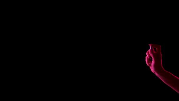 Womans mano spray dito profumo su sfondo nero con luce al neon rosa. Piccola particella di eau de toilette disperdersi nello spazio. Spray di Colonia isolato al buio con retroilluminazione. Chiudete. Rallentatore. — Video Stock