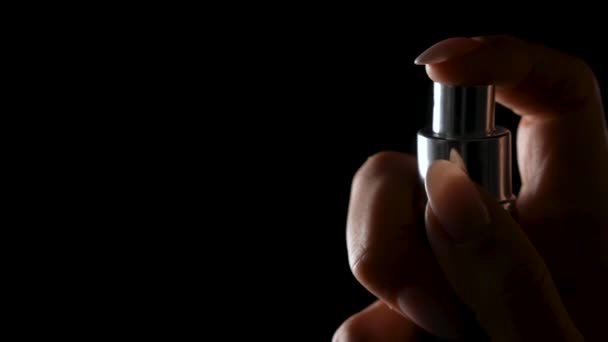 Vrouwen handvinger sprays parfum op zwarte achtergrond. Kleine deeltjes eau de toilette verspreiden zich in de ruimte. Keulen spray geïsoleerd in het donker met achtergrondverlichting. Sluit maar af. Langzame beweging. — Stockvideo