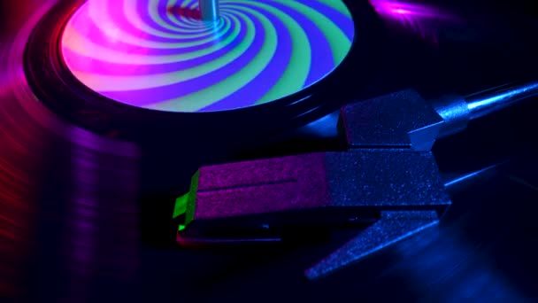 Top view of turntable needle on vinyl record close up illuminated with bright neon lights. Vinyl record spins in gramophone music player and plays an old disco. Popular 80s disco styles. Slow motion. — Wideo stockowe