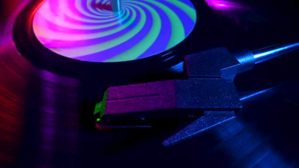 Top view of turntable needle on vinyl record close up illuminated with bright neon lights. Vinyl record spins in gramophone music player and plays an old disco. Popular 80s disco styles. Slow motion. — Wideo stockowe