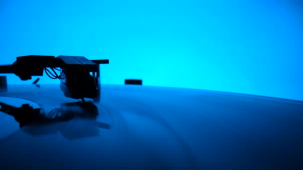 Disco in vinile che gira sul classico lettore di grammofoni su uno sfondo blu colorato. Il giradischi in vinile suona musica. Chiudere ago riproducendo un record nei raggi di luce blu al neon. Rallentatore. — Video Stock