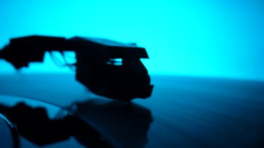 Music retro turntable with spinning vinyl record against backdrop of blue lights. Camera focuses on the turntable needle on vinyl record, then moves away and the picture becomes blurry. Slow motion.