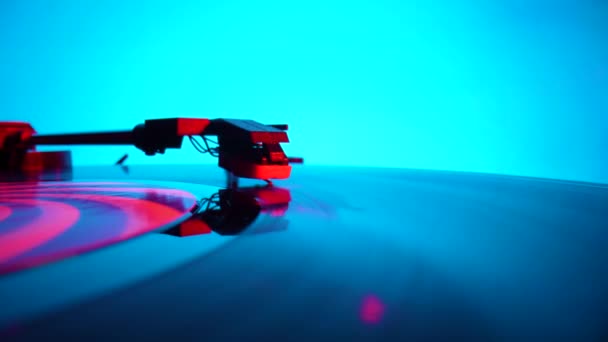 Black vinyl record spinning and play music on old turntable in rays of bright red and blue neon lights. Turntable needle on vinyl record, reads recording from grooves on disc. Close up. Slow motion. — Stockvideo