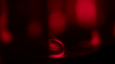Professional stage lighting equipment emitting red beams of light against a dark studio background with clouds of smoke. Red spotlight in a smoky dark nightclub during a party. Close up. Slow motion.