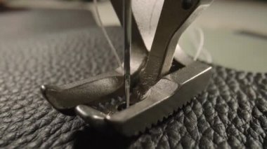 Macro shot of sewing machine needle with thread and presser foot tailoring leather piece during sewing process in handmade workshop. Slow motion of production operation. Sewing equipment close up.