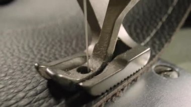 Macro shot of sewing machine needle with thread and presser foot tailoring leather piece during sewing process in handmade workshop. Slow motion of production operation. Sewing equipment close up.