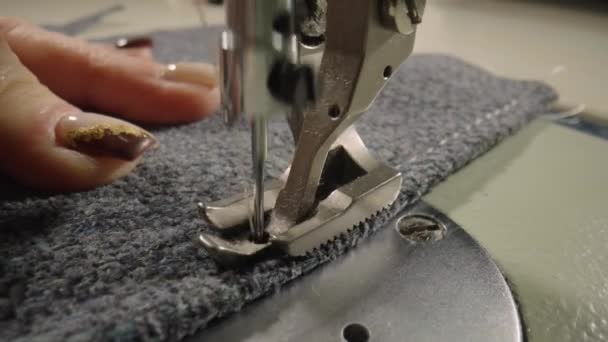 Seamstress sews woolen fabric on sewing machine, advances fabric with his fingers. Movement of foot and needle with thread when sewing on sewing machine. Slow motion of production operation. Close up. — Stock video