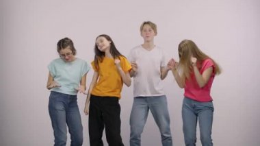 A group of cute young people looking at the camera with surprise and wow delight, then dancing and having fun. Guy and three girls models posing on a white background in the studio.