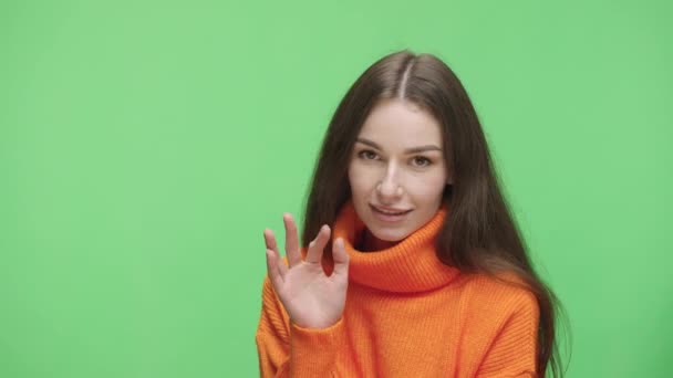 Portrait of young girl looking coquettishly at camera, waving hello, making air kiss and heart sign. Model girl posing in studio against background of green screen chroma key. Close up. Slow motion. — Αρχείο Βίντεο