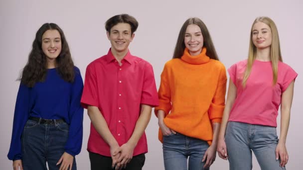 A group of young people looking at the camera and at each other and smiling happily. A guy and three girls models are posing on a white background in the studio. Close up. Slow motion. — Wideo stockowe