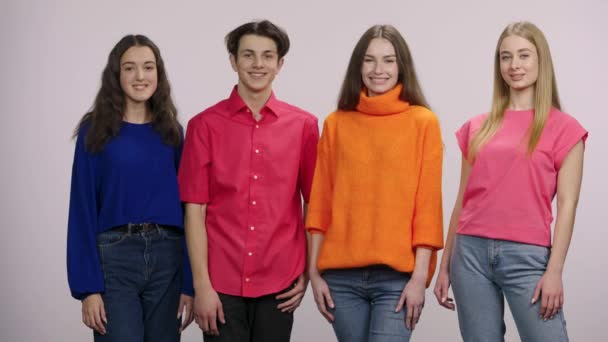 A group of young people looking at the camera, smiling joyfully and showing a thumbs up, like gesture. A guy and three girls models are posing on white background in the studio. Close up. Slow motion. — Αρχείο Βίντεο