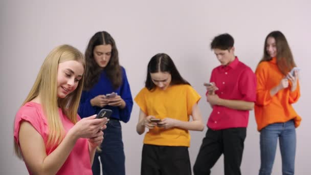 Group of handsome young people are chatting using a mobile phone or browsing information on social networks. Guy and four girls models posing on a white background in the studio. Close up. Slow motion — Vídeo de Stock