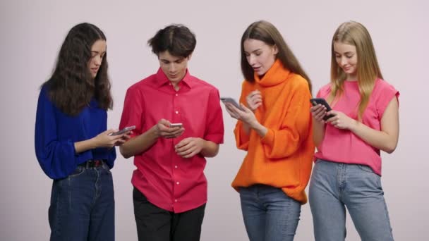 A group of handsome young people are texting with a mobile phone. Guy and three girls models posing on a white background in the studio. Close up. Slow motion. — Vídeo de Stock