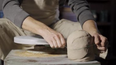 Tanınmayan bir erkek çömlekçi yumuşak bir kil parçasını iplikle keser ve çömlekçi çarkında modellik yapmak için top oluşturur. Çömlekçilik kapanış aşamasında. Ağır çekimde kil yontuyorum..