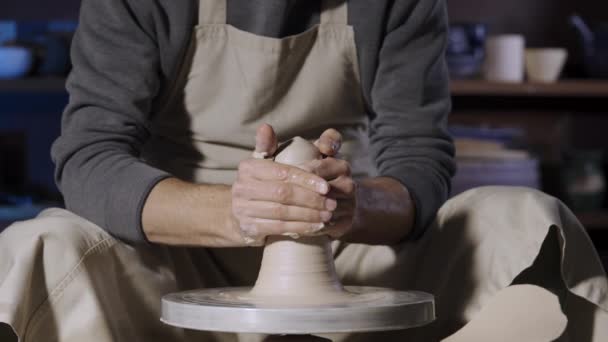 Potter rzeźbi miękką białą glinę mokrymi rękami, obracając się na kole garncarskim. Kształtowanie i rzeźbienie gliny, zamykanie ręcznej pracy twórczej w warsztacie pracy. Przetwarzanie materiałów ceramicznych w zwolnionym tempie. — Wideo stockowe