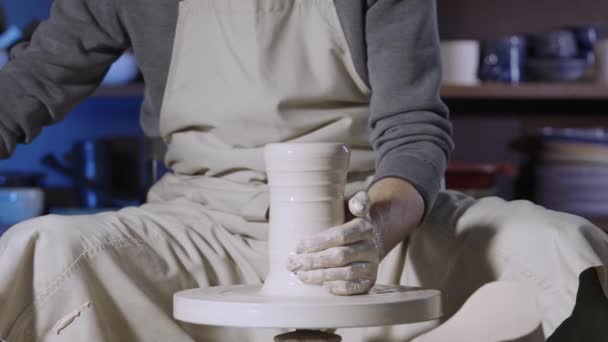 Las manos masculinas de los alfareros forman y esculpen la olla de arcilla blanca suave, girando sobre una rueda de alfarero en un taller creativo. Maestro da forma diferente a la cerámica. Clay dando forma de cerca. Movimiento lento. — Vídeo de stock