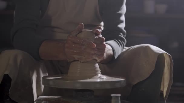 The potters male hands shape and sculpt the soft white clay pot, spinning on a potters wheel in a creative workshop. Master gives different shape to the pottery. Clay shaping close up. Slow motion. — Stock Video