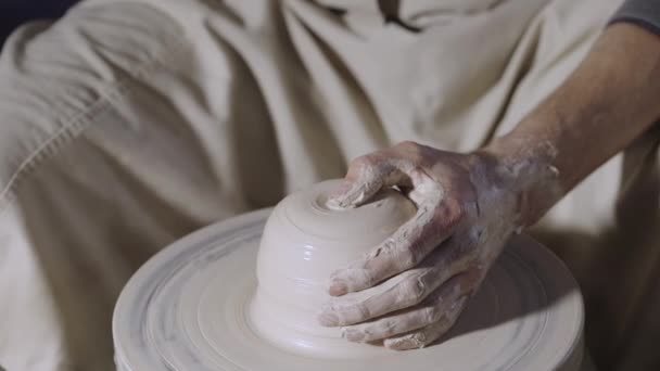 Männliche Töpferhände formen und formen den weichen weißen Tontopf, der sich in einer Kreativwerkstatt auf einer Töpferscheibe dreht. Der Meister gibt der Keramik eine Form. Tonformung aus nächster Nähe. Zeitlupe.