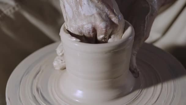 制陶工人的男性手塑造和雕刻柔软的白土罐子，在一个创造性的车间里在一个陶工轮上旋转。主人使陶器成形了.粘土的形状接近。慢动作. — 图库视频影像