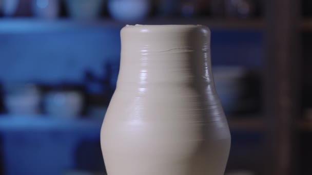 一种形状柔软的白色粘土陶器，在一个创造性的作坊中旋转在陶瓷轮上。陶壶由陶工亲手铸成的壶陶器在柔和的光线下密闭着.慢动作. — 图库视频影像
