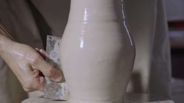 男性陶工的手利用陶器工具形成了一个柔软的白土罐子，在一个创造性的车间里把它放在一个陶工的轮子上。主人使陶器成形了.粘土的形状接近。慢动作. — 图库视频影像