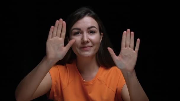 Portrait of an excited young girl banging her fists and palms on the glass, waving hello and gesturing I am here. Model girl posing on a black background in the studio. Close up. Slow motion. — Stock Video