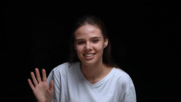 Portrait of an excited young girl banging her fists and palms on the glass and waving hello. Model girl posing on a black background in the studio. Close up. Slow motion. — Stock Video
