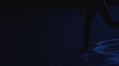 Genç bayan artistik patinajcı, yumuşak mavi ışığa karşı buz pistinde tek kişilik bir kadın paten koreografisi yapıyor. Bacak sanatsal patinajcısı, buz üstünde kayma ve dönme alıştırması yapıyor. Ağır çekim. Kapat..