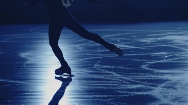 A jovem patinadora feminina está realizando uma coreografia de patinação única feminina na pista de gelo contra a luz azul suave. Pernas patinador artístico, praticando deslizamento e rotação no gelo. Movimento lento. Fechar. — Vídeo de Stock