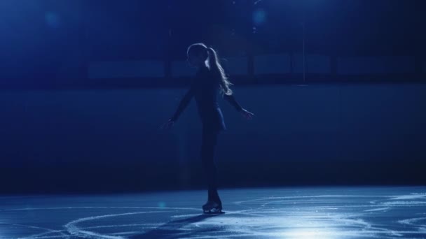 Художественная фигуристка исполняет одиночную хореографию на катке против мягкого синего света. Силуэт спортсмена, выполняющего вращение на одной ноге. Медленное вращение фигурного катания — стоковое видео