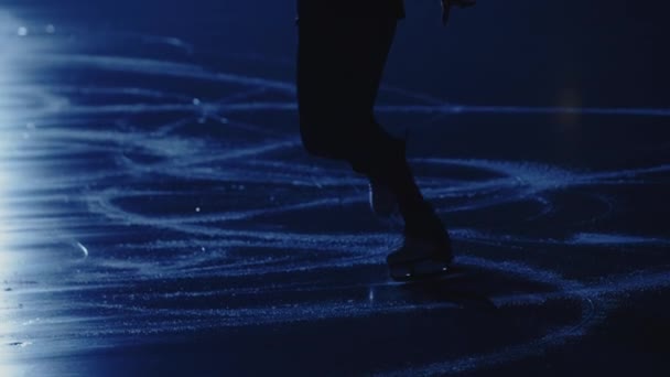 Joven patinadora artística femenina está realizando una coreografía de patinaje individual femenina en pista de hielo contra la luz azul suave. Patas patinador artístico, la práctica de deslizamiento y rotación sobre hielo. En cámara lenta. De cerca.. — Vídeos de Stock