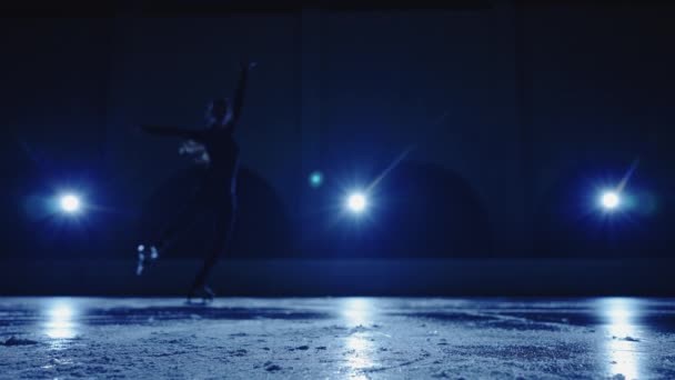 Silhouette floue de la jeune patineuse artistique effectue une chorégraphie de patinage unique sur la patinoire contre la lumière bleue douce. Athlète femme pratiquant des compétences de glissement et de filature. Mouvement lent. — Video