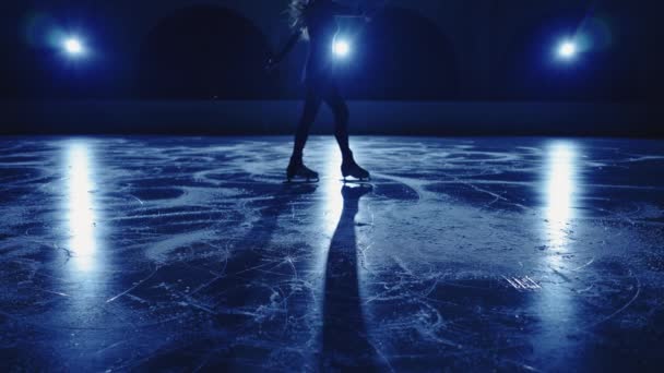 Размытый силуэт юной фигуристки исполняет одиночную хореографию на ледовой арене против мягкого синего света. Спортсменка, практикующая скольжение и вращение. Медленное движение. — стоковое видео